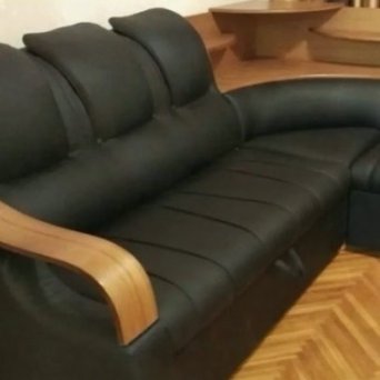 Кожаный, черный, угловой диван стоит в углу комнаты. Диван выглядит новым. Фото сделано после того, как компания Мастерская Мебели 48 произвела  перетяжку новым материалом-черной кожей.