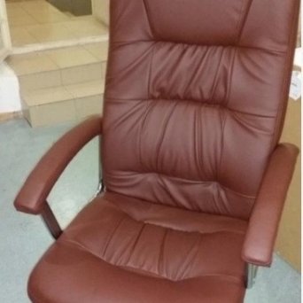 Кожаное коричневое офисное кресло стоит в помещении офиса. Оно выглядит новым после того, как Мастерская Мебели 48 осуществила недорогой ремонт этого кресла.