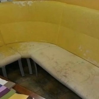 Желтый кухонный уголок стоит на кухне в углу. На столе перед ним образцы тканей для обивки. До ремонта.