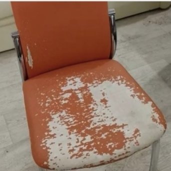 Оранжевый стул, из кожзама, с вытертым сидением стоит  на полу, покрытым светлым ламинатом